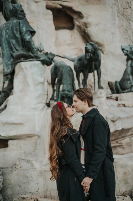 Budapest couple photoshoot with a kiss beside the castle fountain Couple kissing in front of the sculpted fountain in the Buda Castle grounds during their photoshoot in Budapest