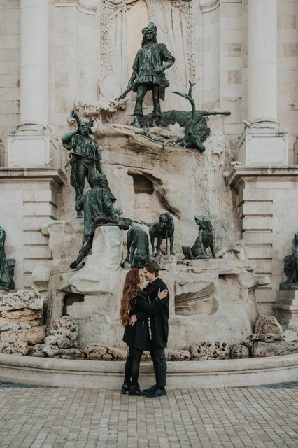 Morning photoshoot in Budapest beneath the castle fountain sculptures Couple sharing a kiss beneath the Buda Castle fountain sculptures during their morning photoshoot in Budapest