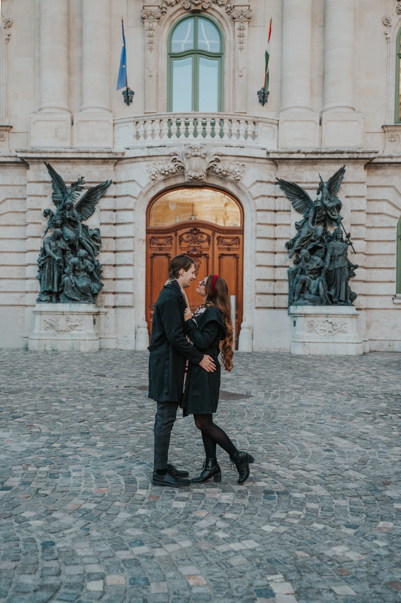 Couple walking together in front of the Buda Castle facade and wooden doorway during their photoshoot in Budapest