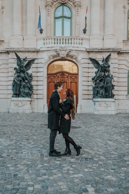 Budapest couple photoshoot walking past the castle facade Couple walking together in front of the Buda Castle facade and wooden doorway during their photoshoot in Budapest