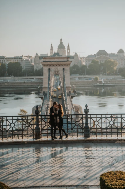 Couple standing close together on a lower Buda Castle platform during their photoshoot in Budapest, with the Chain Bridge in the backdrop