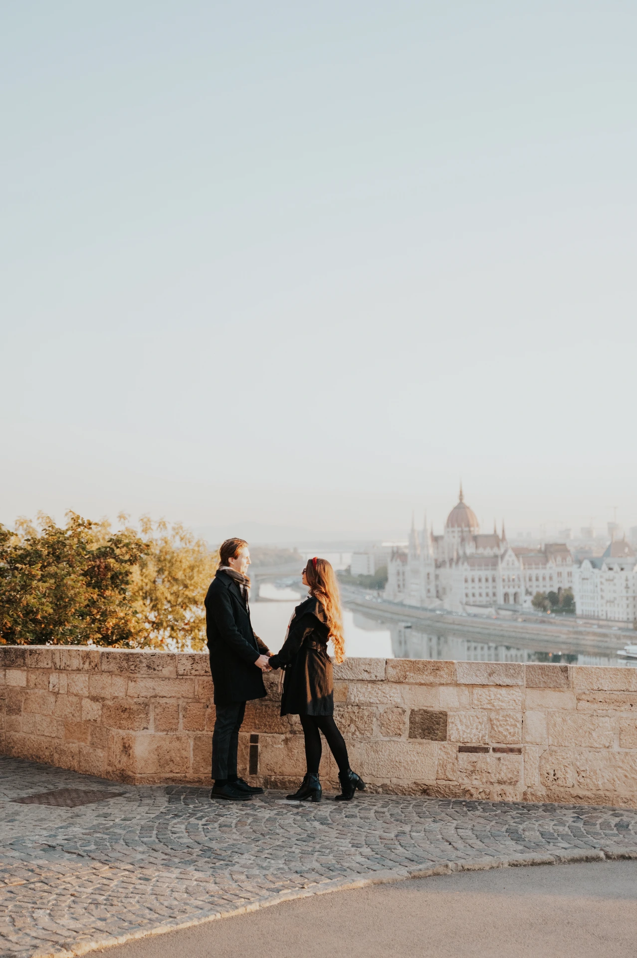 Couple sharing a kiss beside the Buda Castle parapet during their Budapest photoshoot, with the city in the background