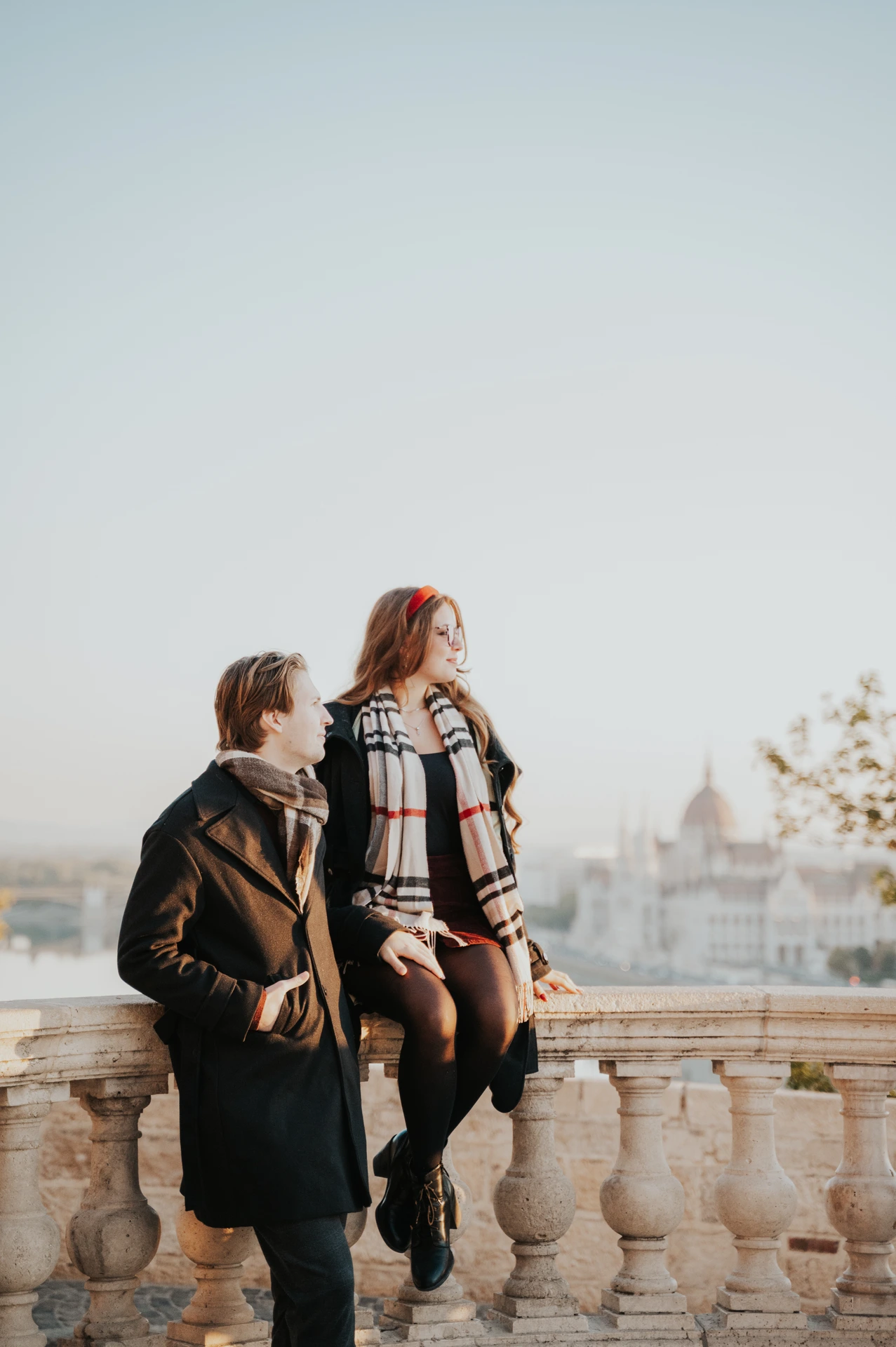 Woman sitting on the Buda Castle balustrade beside her partner during their couple photoshoot in Budapest
