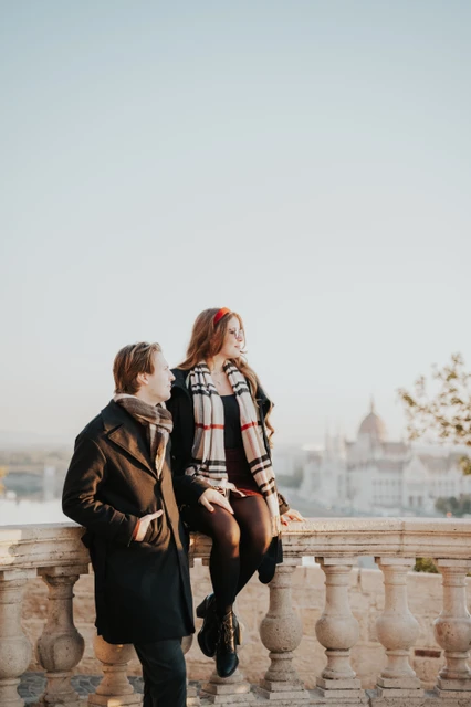 Relaxed couple photoshoot in Budapest at the castle balustrade Woman sitting on the Buda Castle balustrade beside her partner during their couple photoshoot in Budapest