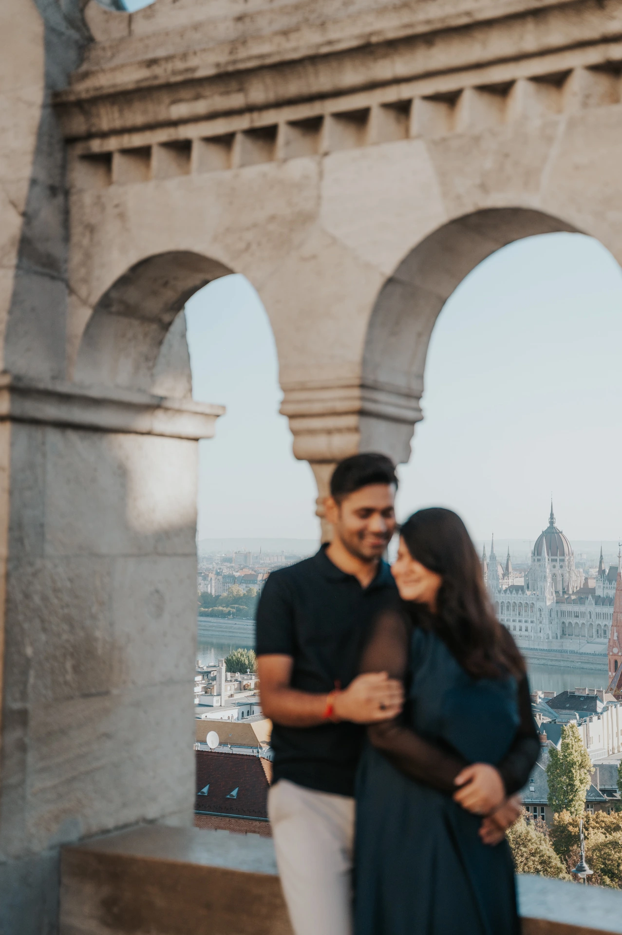 The couple laughing together in front of an open stone arch at Fisherman’s Bastion during a couple photoshoot in Budapest.