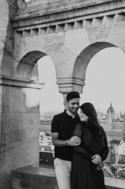 Budapest couple photoshoot: a close moment beside the open arcade in black and white Black-and-white photograph of the couple leaning close together beside the open arcade at Fisherman’s Bastion during a couple photoshoot in Budapest.