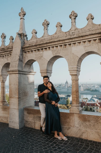 Budapest couple photoshoot: an embrace beside the ornate arcade The man embracing his partner from behind beside the open arcade at Fisherman’s Bastion during a couple photoshoot in Budapest.