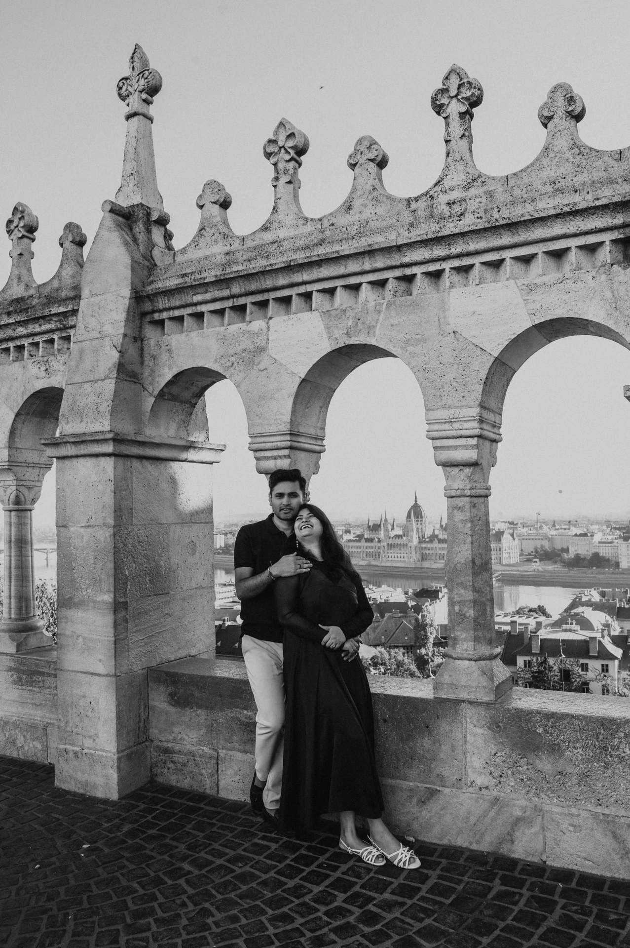 Black-and-white photograph of the couple standing close beside the stone arches and city views at Fisherman’s Bastion during a couple photoshoot in Budapest.