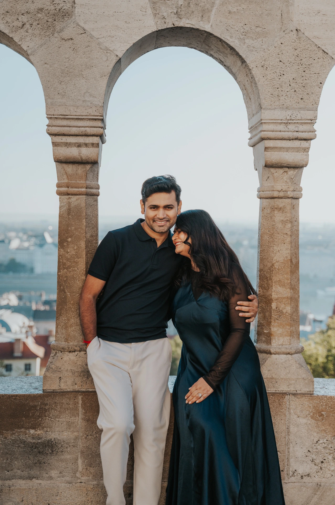The smiling couple leaning close beneath a stone arch at Fisherman’s Bastion during a couple photoshoot in Budapest.