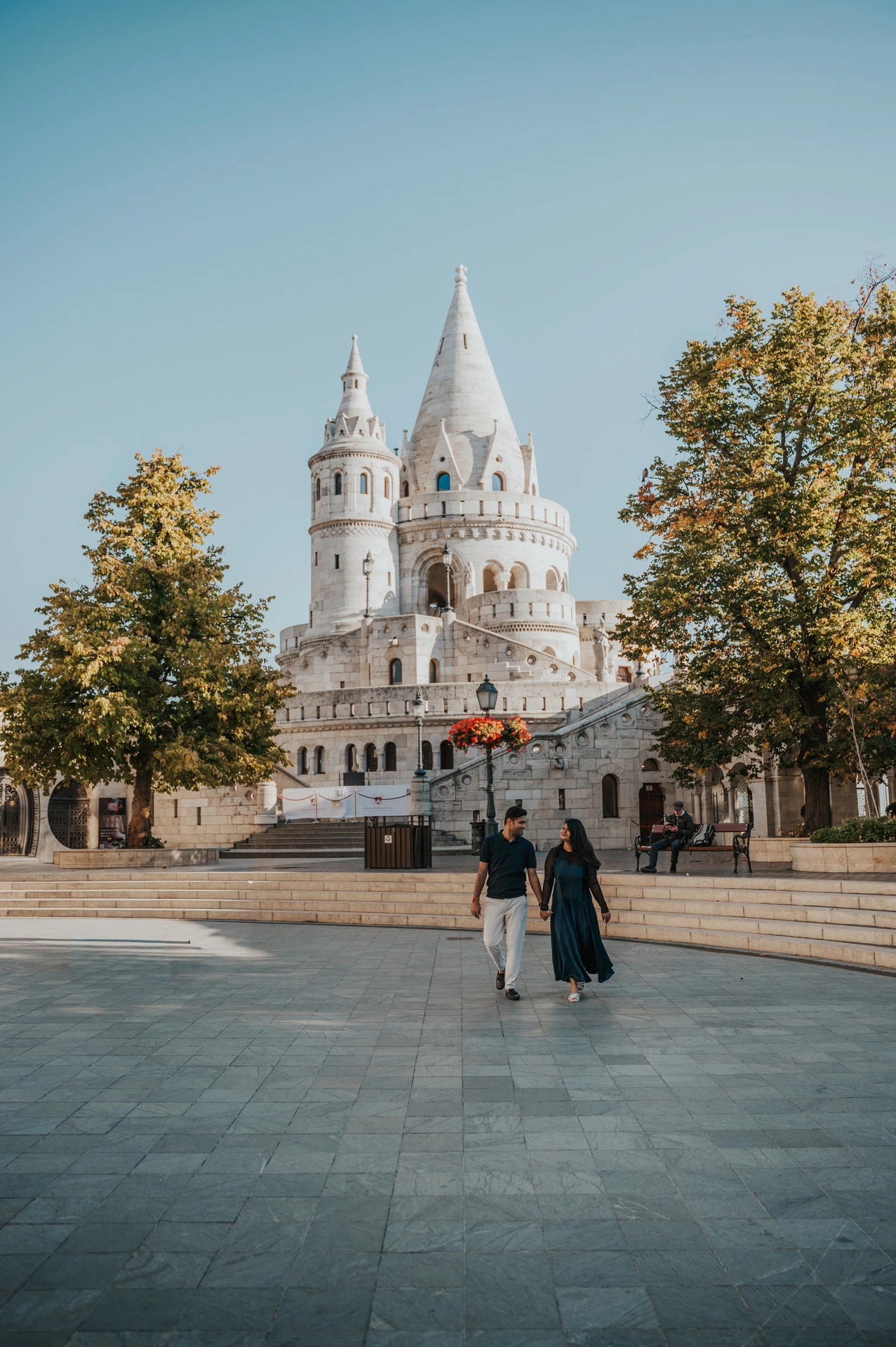 The couple standing in the open square with the towers and arcades of Fisherman’s Bastion behind them during a couple photoshoot in Budapest.