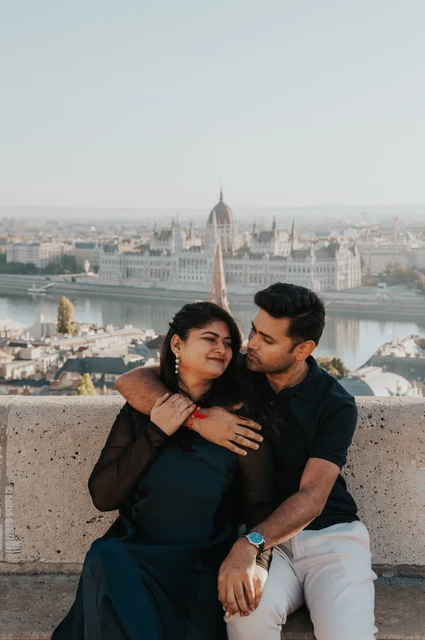 Budapest couple photoshoot: a close portrait above the city The couple sitting close on a stone bench with the city skyline behind them during a couple photoshoot in Budapest.