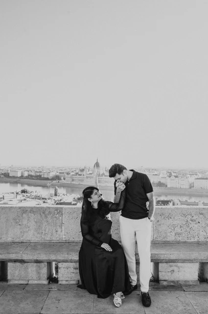 Budapest couple photoshoot: a hand kiss by the Bastion’s stone bench in black and white Black-and-white photograph of the man kissing his partner’s hand beside the stone bench at Fisherman’s Bastion during a couple photoshoot in Budapest.