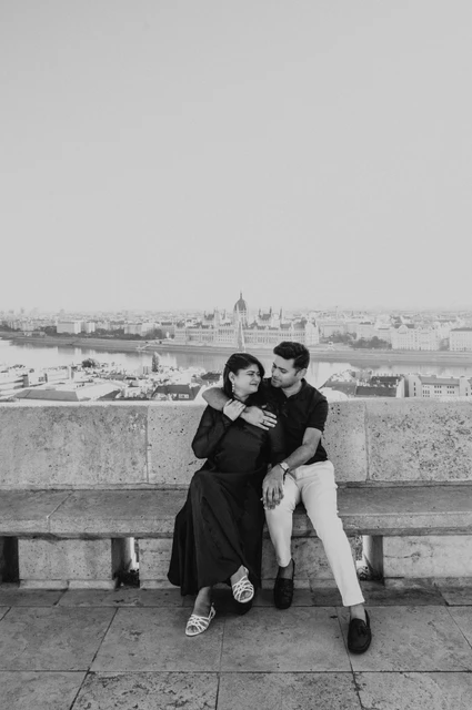 Budapest couple photoshoot: sitting above the city at Fisherman’s Bastion in black and white Black-and-white photograph of the couple sitting together on a stone bench overlooking the city from Fisherman’s Bastion during a couple photoshoot in Budapest.