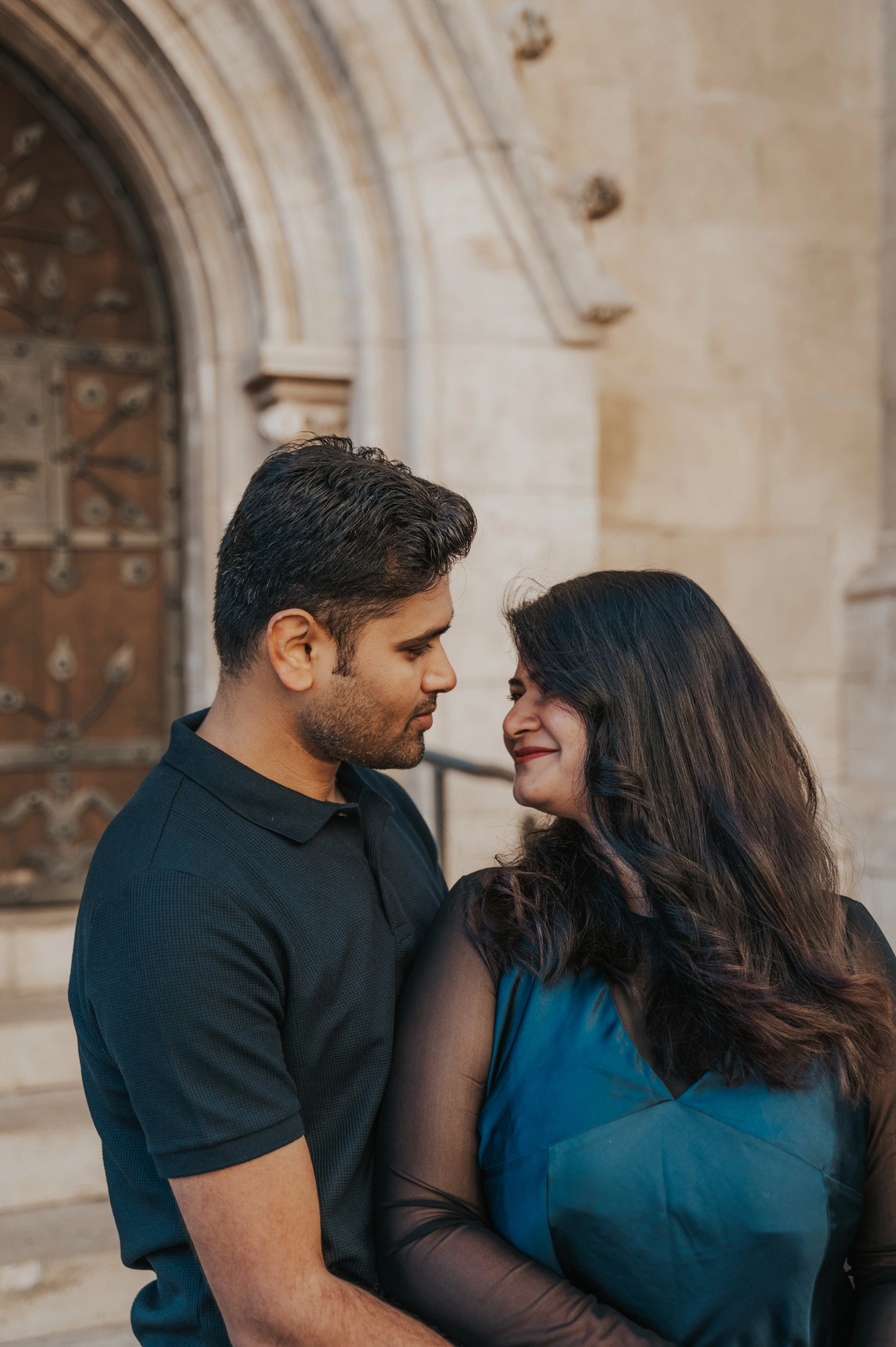 A close portrait of the couple looking towards each other with a pointed church doorway behind them during a couple photoshoot in Budapest.