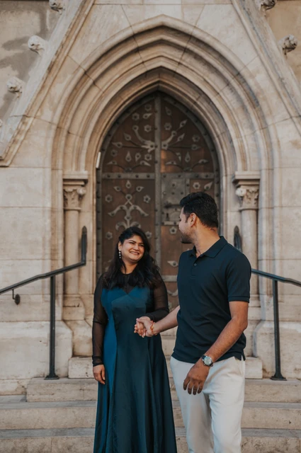 Budapest couple photoshoot: holding hands beneath a church arch The couple holding hands in front of the carved wooden door and pointed arch at Matthias Church during a couple photoshoot in Budapest.