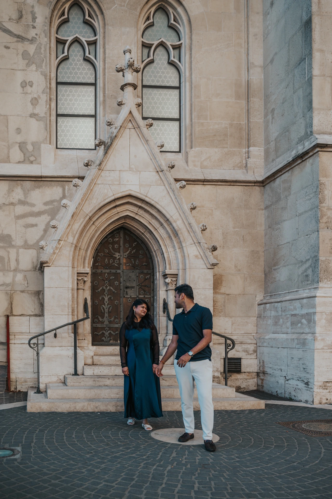 The couple holding hands as they step away from a carved doorway at Matthias Church during a couple photoshoot in Budapest.