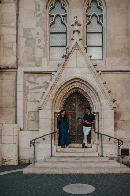 Budapest couple photoshoot: a pointed church doorway and broad steps The couple standing apart on the steps beneath a pointed doorway at Matthias Church during a couple photoshoot in Budapest.