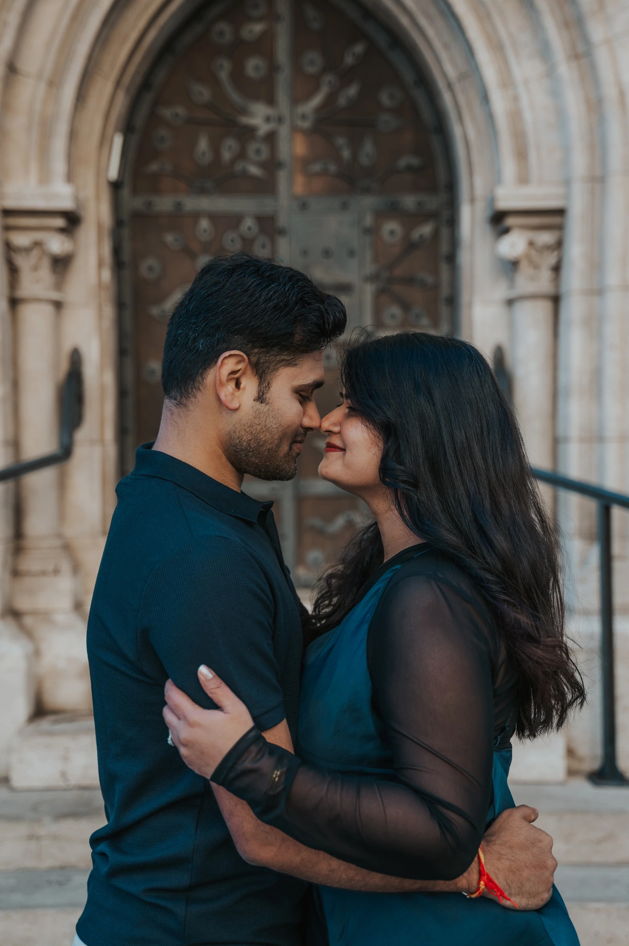 The man kissing his partner’s forehead beside the carved doorway at Matthias Church during a couple photoshoot in Budapest.