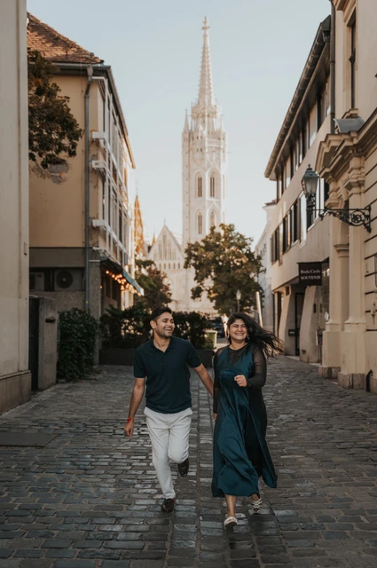 Budapest couple photoshoot: a cobbled street and the church spire The couple walking along a cobbled street with Matthias Church’s spire behind them during a couple photoshoot in Budapest.