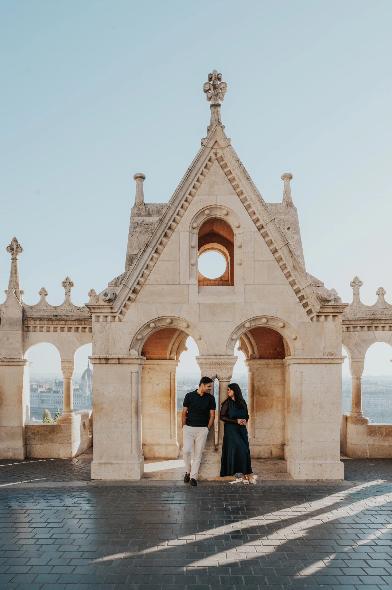 The couple standing together beneath the ornate gabled stonework at Fisherman’s Bastion during a couple photoshoot in Budapest.
