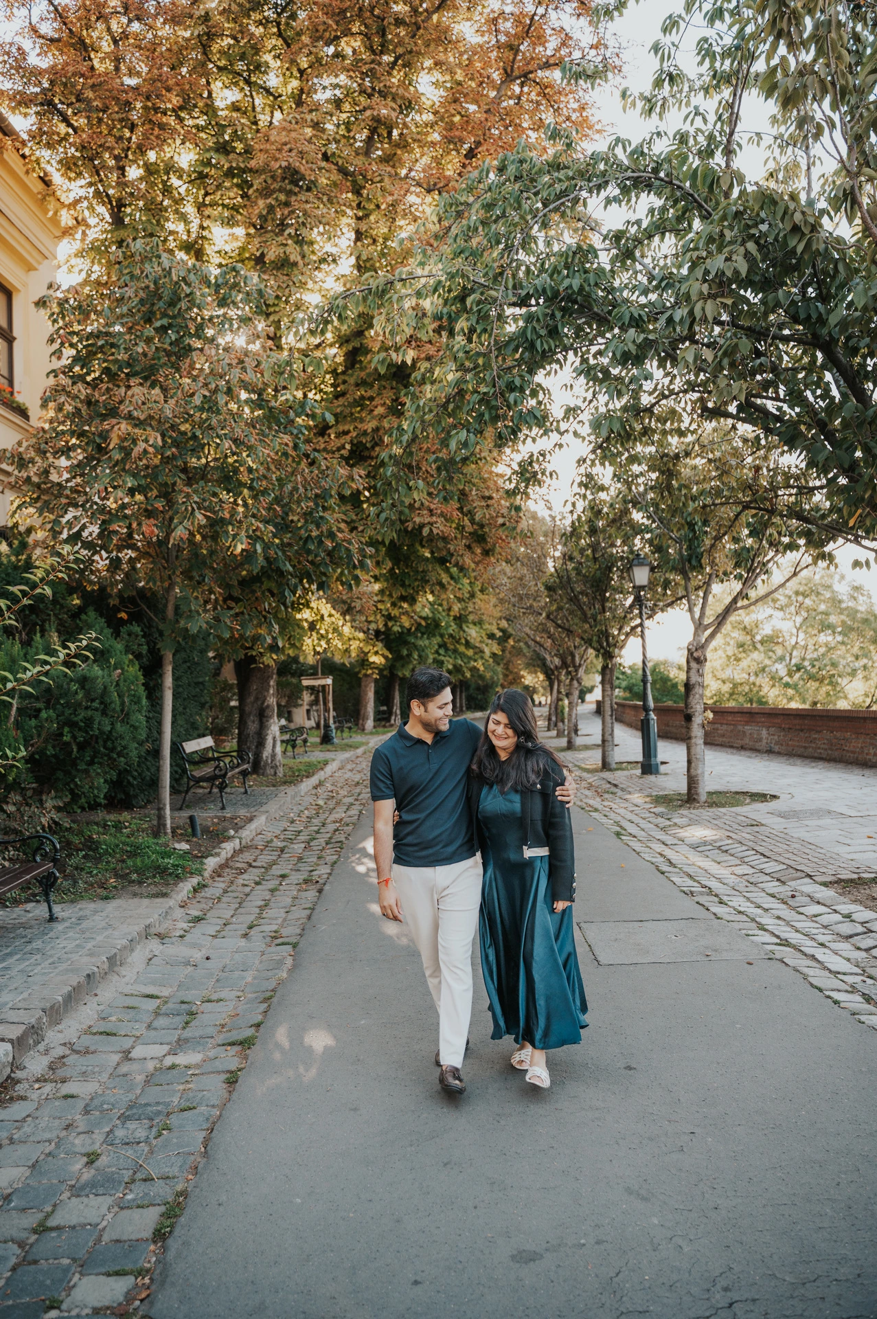 The couple walking hand in hand along Tóth Árpád promenade beneath the leafy trees during a couple photoshoot in Budapest.