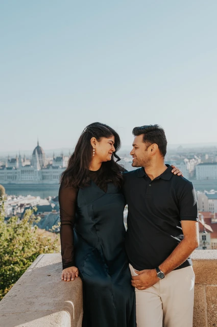 Budapest couple photoshoot: a close portrait with Parliament beyond The couple looking towards each other beside a stone terrace railing with Parliament across the city during a couple photoshoot in Budapest.