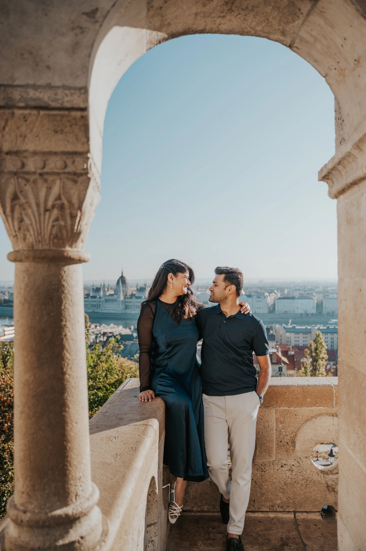 The couple holding hands beneath a stone arch on a terrace at Fisherman’s Bastion during a couple photoshoot in Budapest.