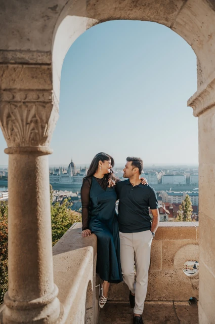 Budapest couple photoshoot: a terrace portrait framed by a stone arch The couple holding hands beneath a stone arch on a terrace at Fisherman’s Bastion during a couple photoshoot in Budapest.