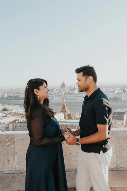 Budapest couple photoshoot: holding hands above the city rooftops The couple holding hands on a terrace at Fisherman’s Bastion with rooftops behind them during a couple photoshoot in Budapest.
