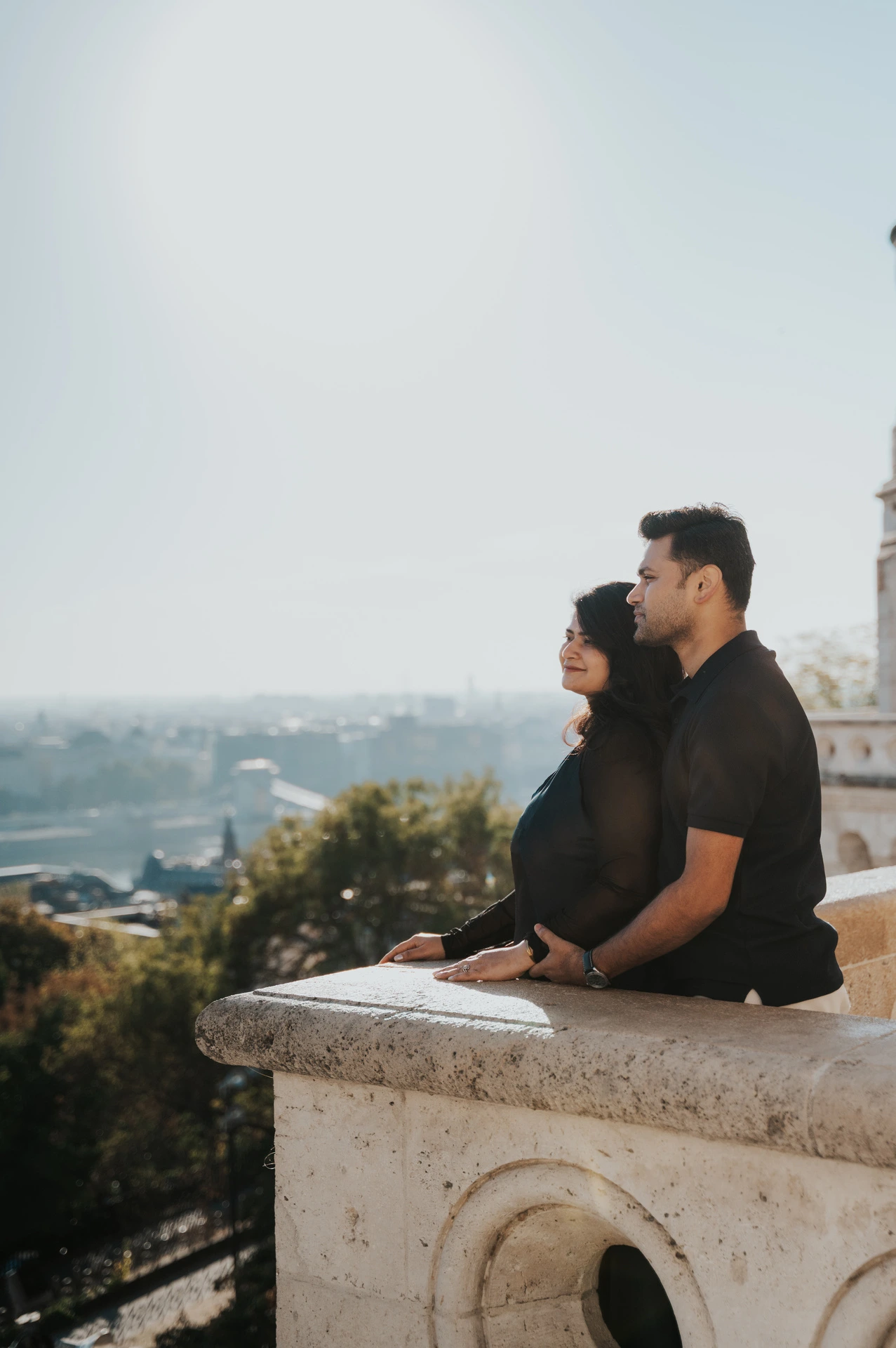 A side view of the couple seated together on the stone terrace above the city at Fisherman’s Bastion during a couple photoshoot in Budapest.