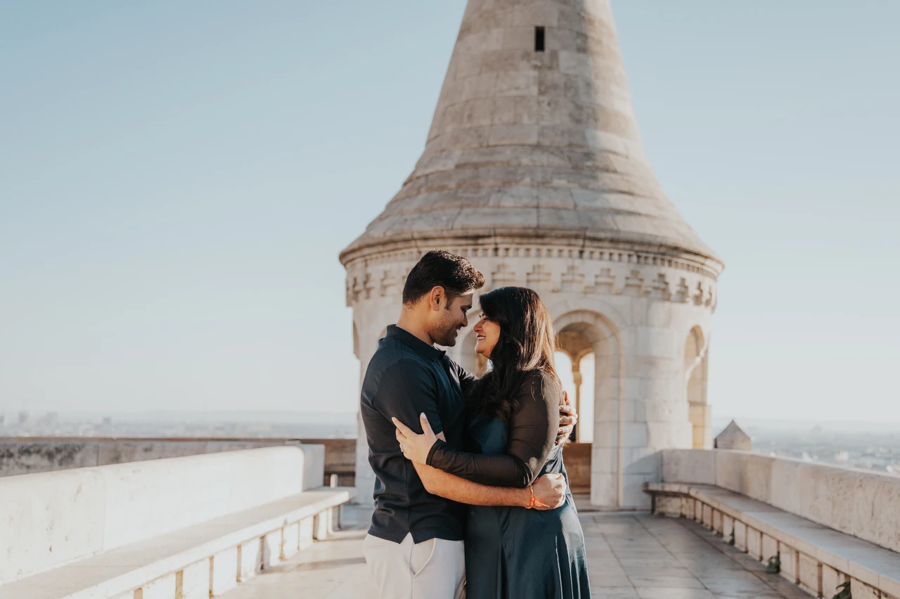 Budapest couple photoshoot: an embrace beside the Bastion tower A landscape portrait of the couple embracing beside a pointed tower at Fisherman’s Bastion during a couple photoshoot in Budapest.