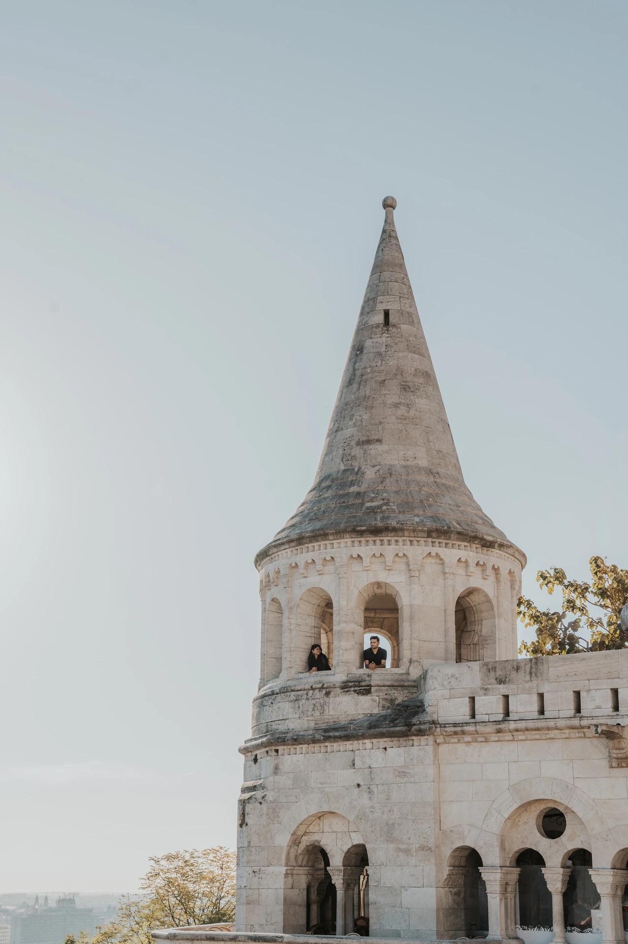 A pointed stone tower at Fisherman’s Bastion rising above the surrounding trees during a couple photoshoot in Budapest.