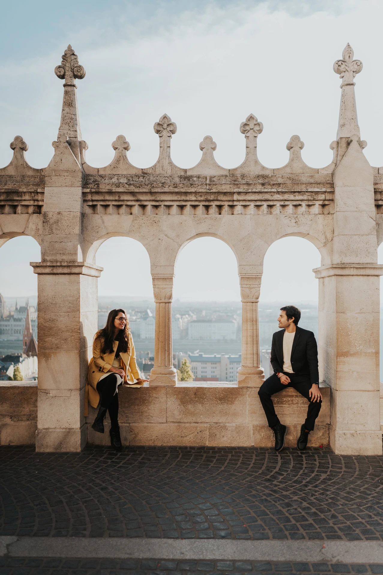 Married couple standing apart beneath the stone arches at Fisherman's Bastion during their morning photoshoot in Budapest