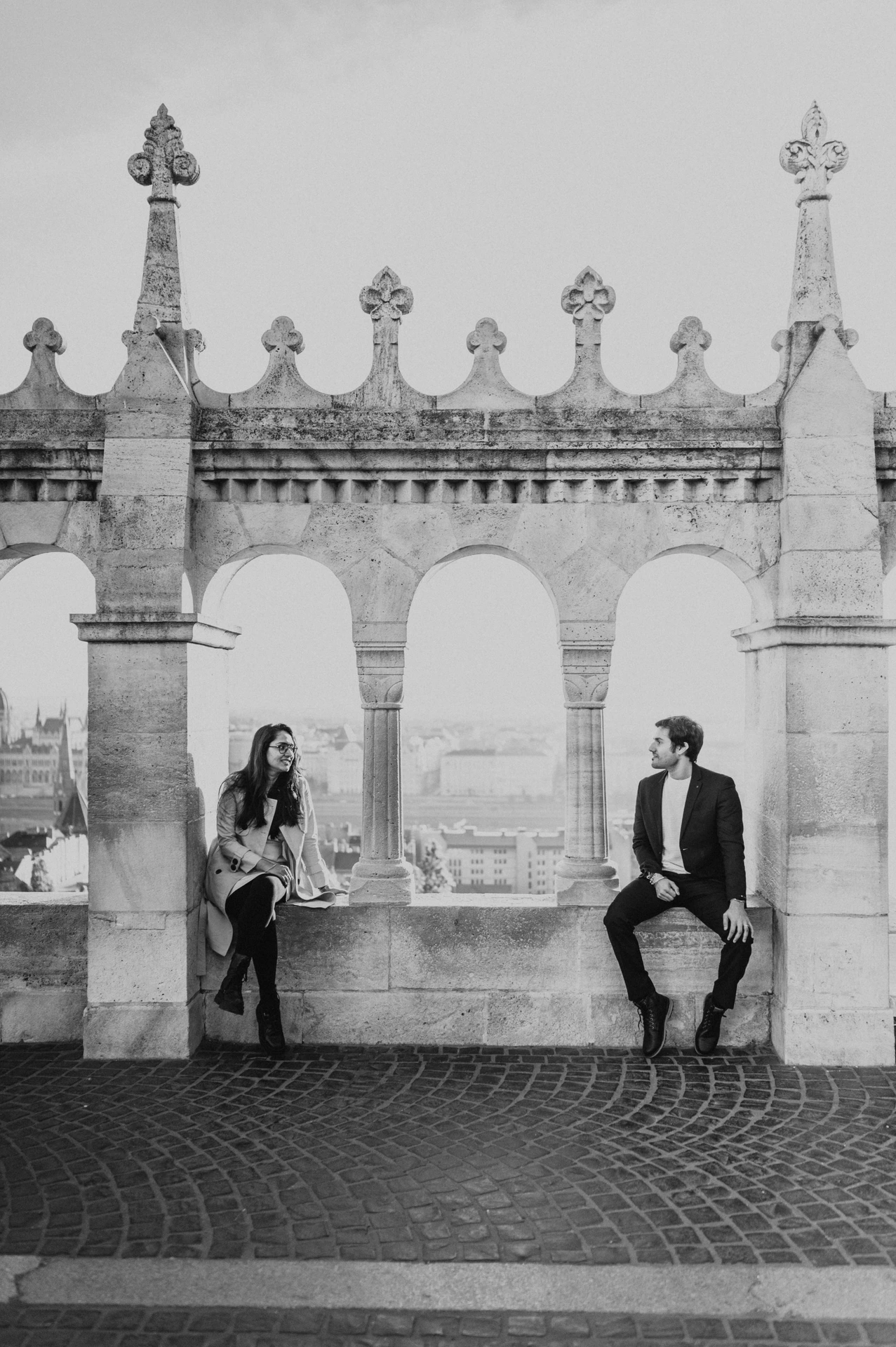 Black and white portrait of a couple beside the arched windows at Fisherman's Bastion during their Budapest photoshoot