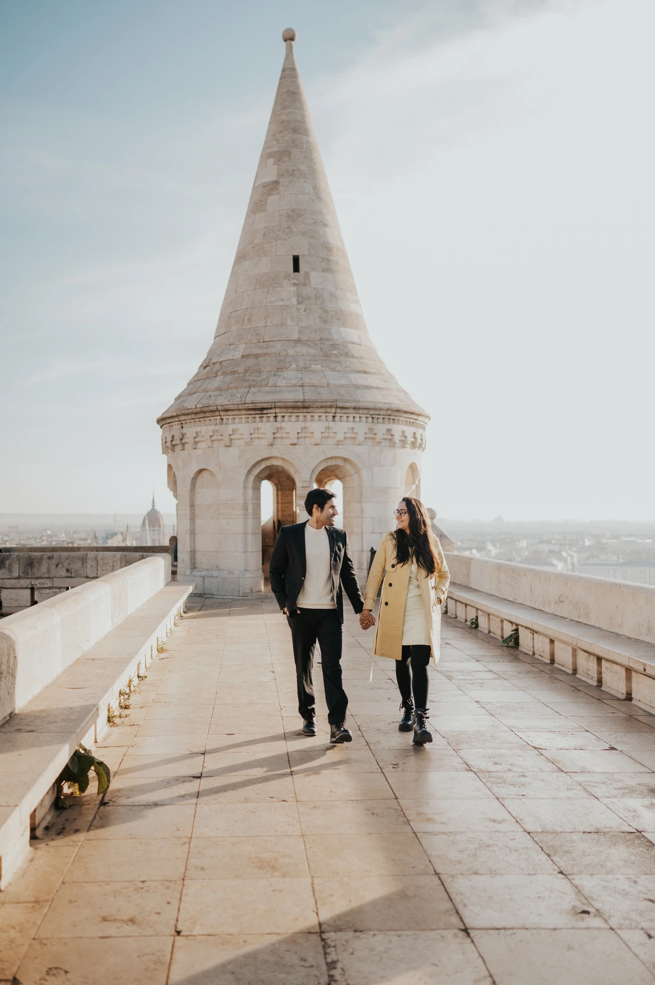 Couple walking hand in hand along the terrace towards a Fisherman's Bastion tower during their Budapest photoshoot