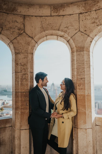 Couple photoshoot in Budapest inside a Fisherman's Bastion window arch Couple smiling towards each other in a stone window arch at Fisherman's Bastion during their Budapest photoshoot