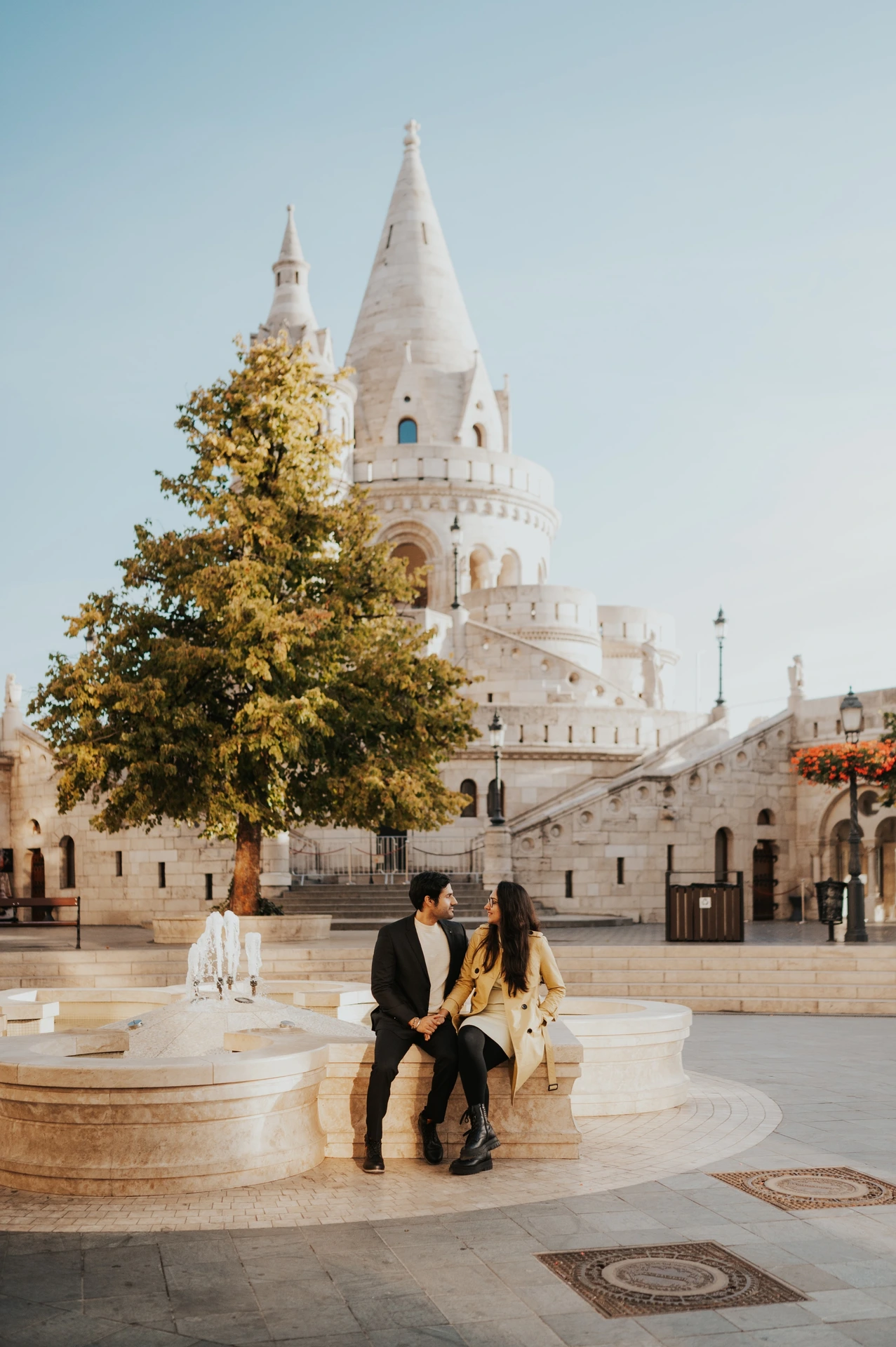 Couple sitting on a curved stone ledge in the square near Fisherman's Bastion during their photoshoot in Budapest