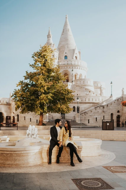 Couple leaning close together on a curved stone ledge near Fisherman's Bastion during their morning photoshoot in Budapest