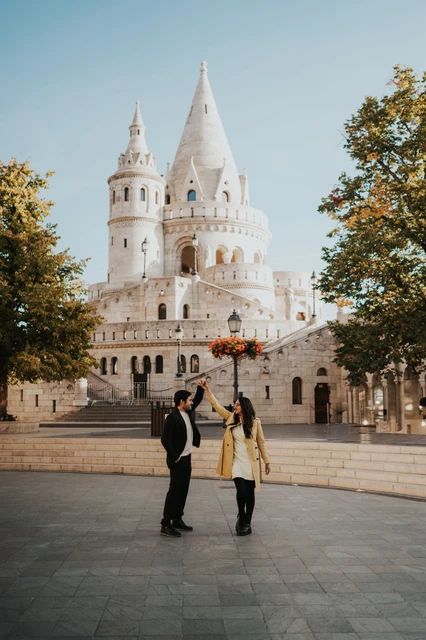 Couple photoshoot in Budapest with a turn in the square by Fisherman's Bastion Man lifting their joined hands as his partner turns in the square near Fisherman's Bastion during their Budapest photoshoot