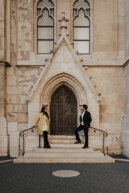 Couple photoshoot in Budapest by the Gothic church doorway near Fisherman's Bastion Couple standing on opposite sides of the steps by an ornate church doorway near Fisherman's Bastion during their photoshoot in Budapest