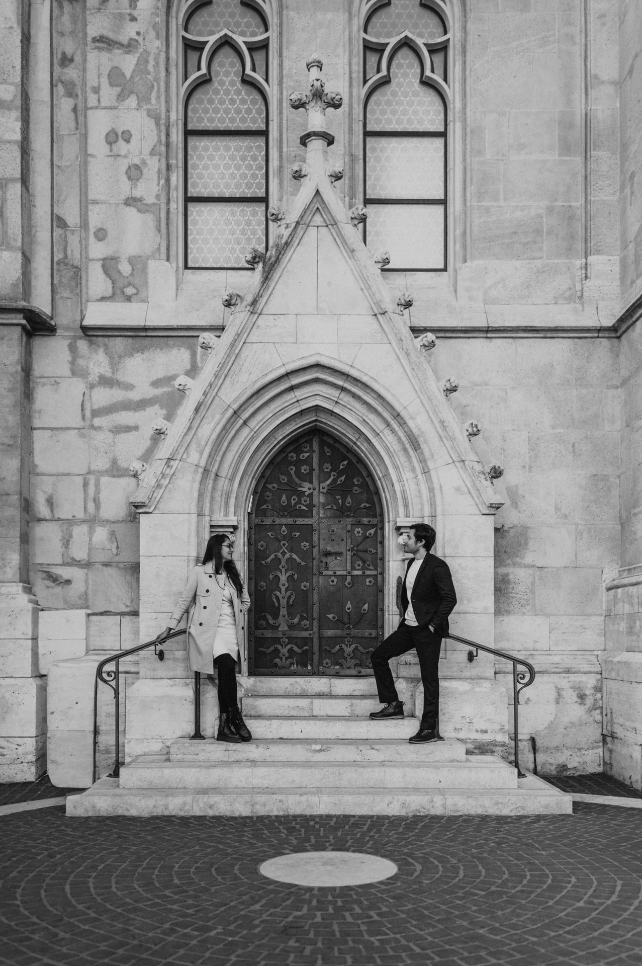 Black and white portrait of a couple on the steps of a Gothic church doorway near Fisherman's Bastion during their Budapest photoshoot