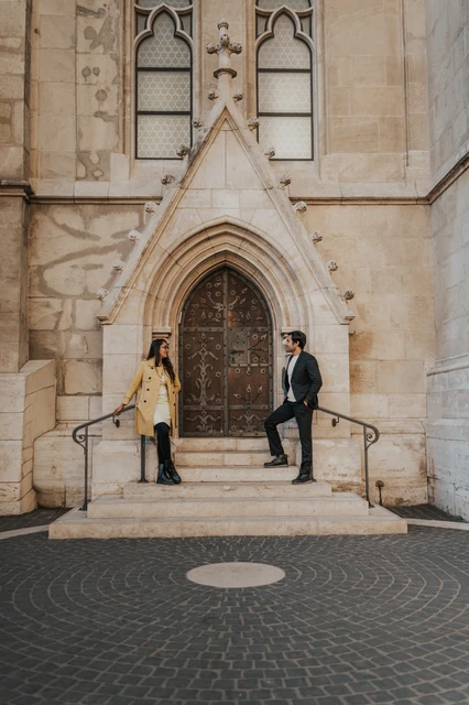 Budapest couple photoshoot on the steps of an ornate church doorway Couple holding hands across the steps in front of an ornate church doorway near Fisherman's Bastion during their Budapest photoshoot