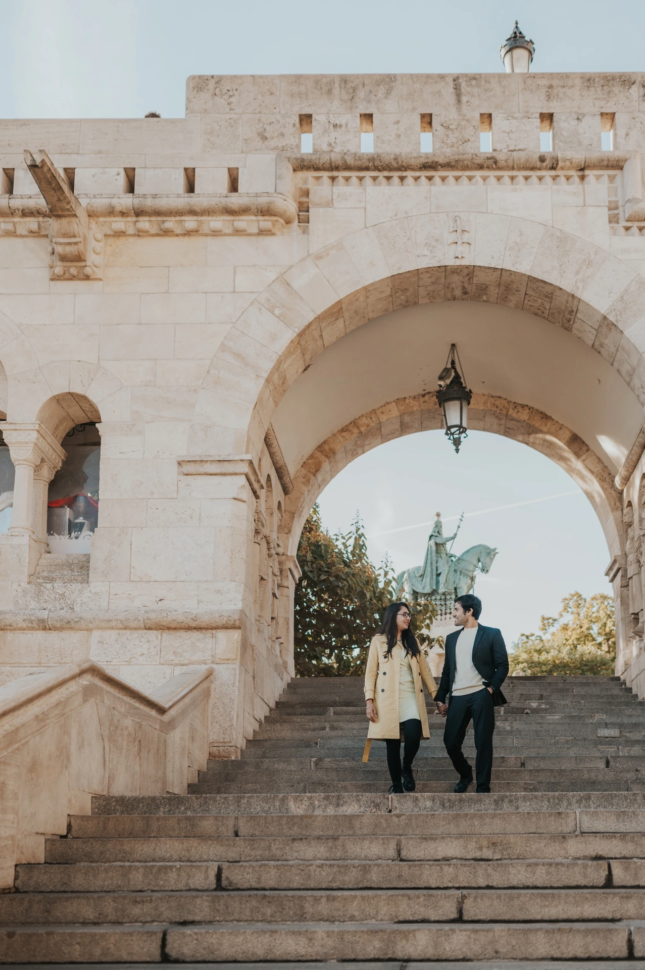 Couple walking down the stone staircase beneath a broad arch at Fisherman's Bastion during their morning photoshoot in Budapest