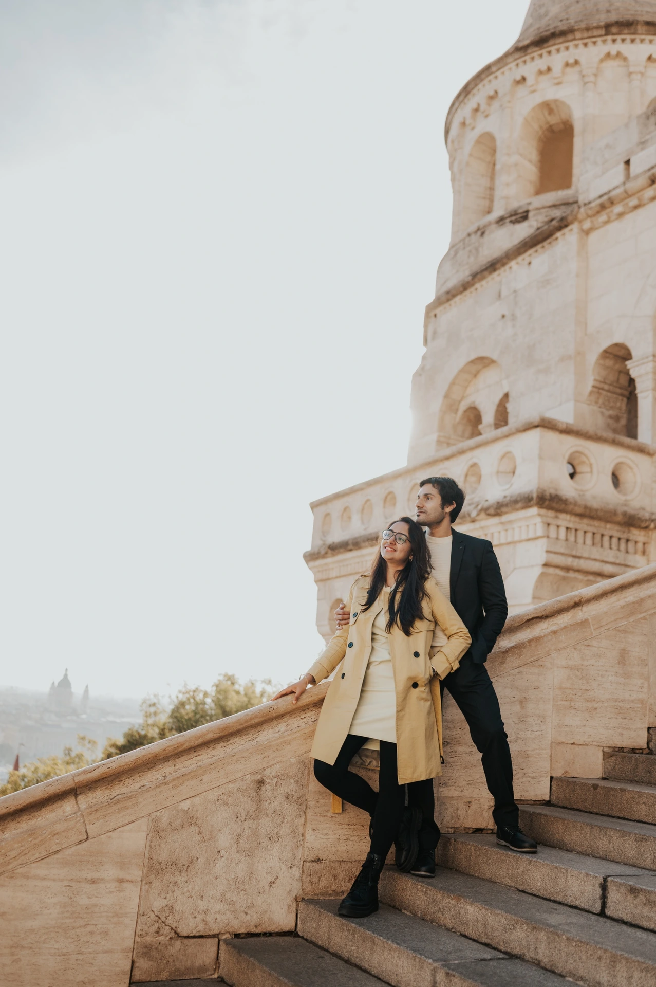 Couple leaning close together on the stone steps beside a Fisherman's Bastion tower during their Budapest photoshoot