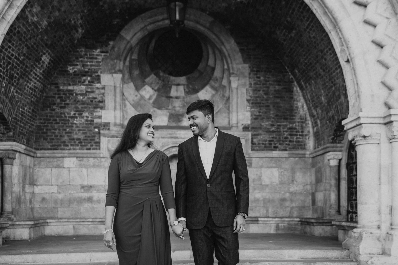 A Budapest couple photoshoot beneath the arch in black and white Black-and-white landscape portrait of the couple smiling at each other beneath the brick-and-stone arch during their Budapest couple photoshoot.