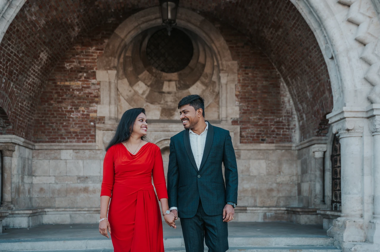 Red and teal beneath the arch at a Budapest couple photoshoot The couple in red and deep teal smiling at each other and holding hands beneath the brick arch during their couple photoshoot in Budapest.