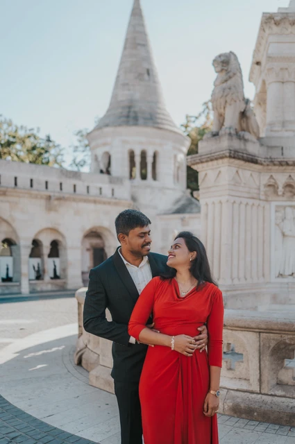 Red and teal beside the turret at a Budapest couple photoshoot The couple in a red dress and deep teal suit standing together with a pointed turret behind them during their Budapest photoshoot at Fisherman’s Bastion.
