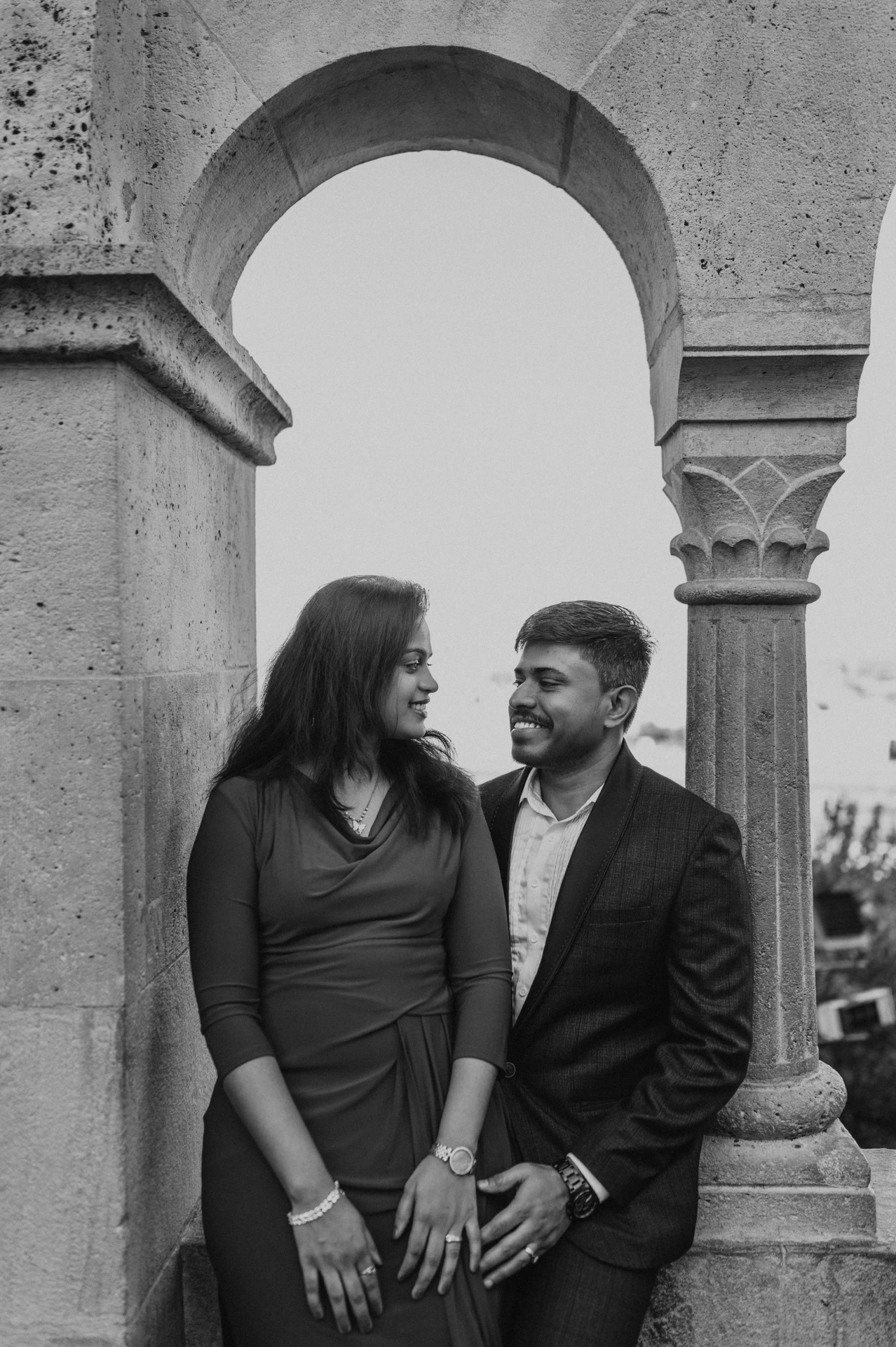 Black-and-white portrait of the couple standing close beneath a stone arch at Fisherman’s Bastion during their couple photoshoot in Budapest.