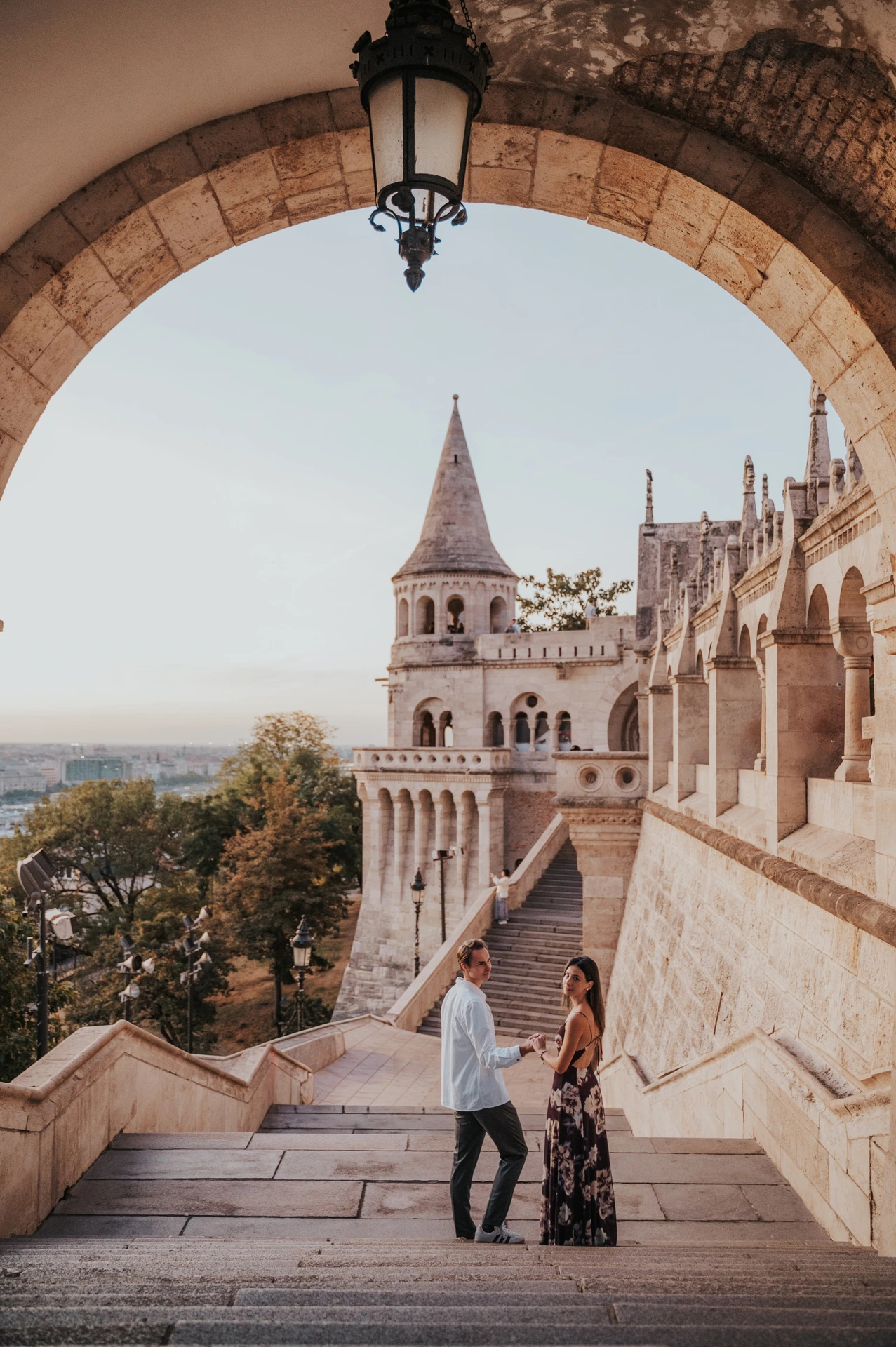 Wide view of the couple on the stone staircase beneath an arch during their Budapest photoshoot at Fisherman’s Bastion.