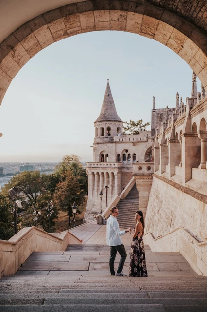 Photoshoot in Budapest beneath a Fisherman’s Bastion arch The couple holding hands on the broad stone steps during their Budapest photoshoot, framed by a curved arch.